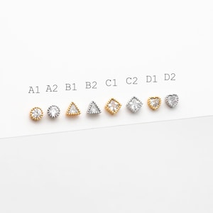 May include: A collection of eight stud earrings in various shapes: round, triangle, square, and heart. The earrings are in gold and silver tones, with clear gemstones. The image includes text labels A1, A2, B1, B2, C1, C2, D1, and D2.