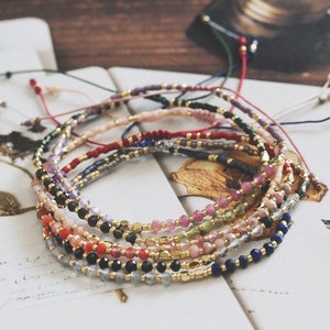 May include: A collection of colorful beaded bracelets with gold accents. The bracelets are made with various gemstones and beads, including amethyst, rose quartz, and lapis lazuli.