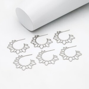 Puede incluir: Cinco pendientes de aro plateados con un delicado dise&ntilde;o floral. Los pendientes est&aacute;n hechos de metal y tienen una forma circular.