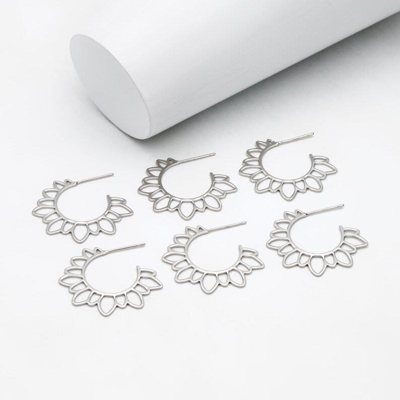 Puede incluir: Cinco pendientes de aro plateados con un delicado dise&ntilde;o floral. Los pendientes est&aacute;n hechos de metal y tienen una forma circular.