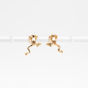 May include: A pair of gold frog earrings. The frogs are facing forward with their legs outstretched.