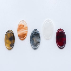 May include: Five oval-shaped resin charms with different marbled patterns. The charms are in shades of brown, white, grey, and red.