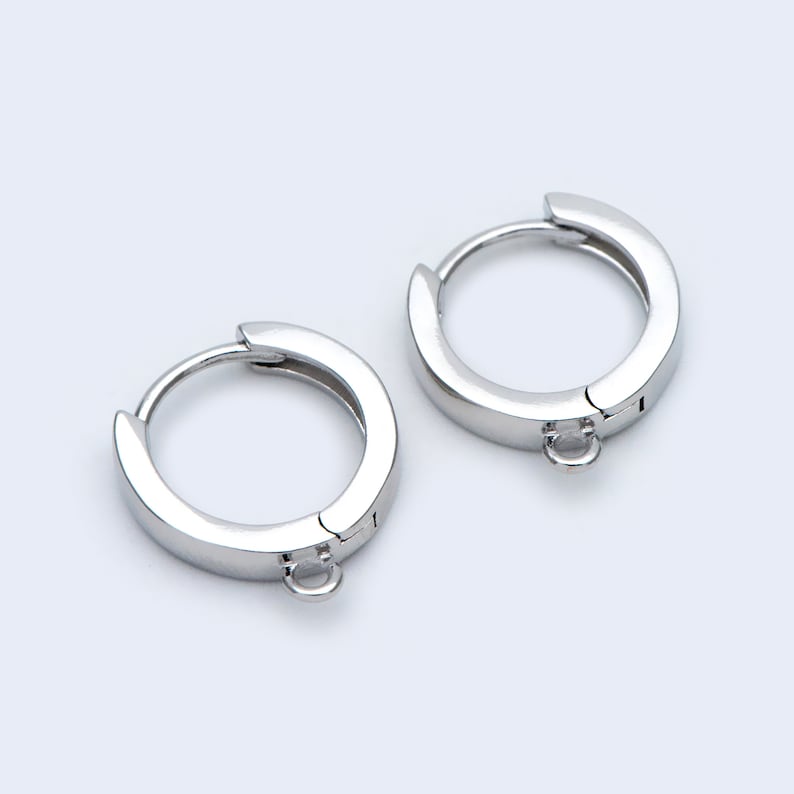 May include: A pair of silver hoop earrings with a small, dangling loop on each earring.