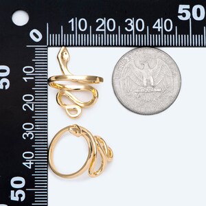 May include: Two gold-coloured snake rings. One ring features a coiled snake design with the snake's head raised. The other ring has a similar coiled snake design. A coin is next to the rings for size comparison.