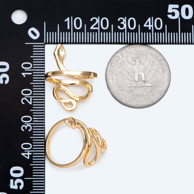 May include: Two gold-coloured snake rings. One ring features a coiled snake design with the snake's head raised. The other ring has a similar coiled snake design. A coin is next to the rings for size comparison.