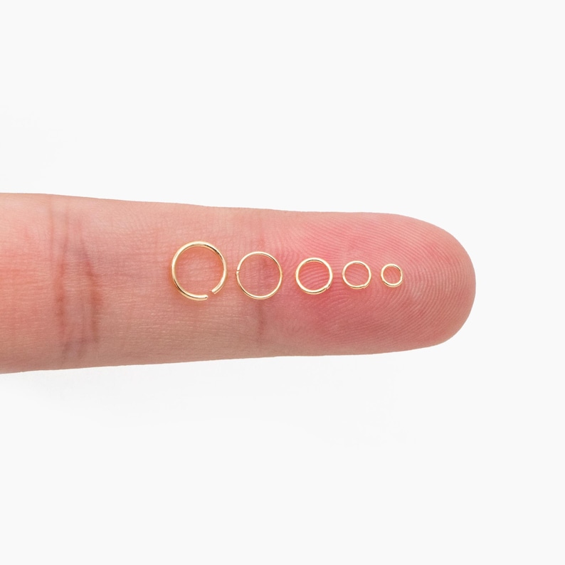 May include: A set of six gold hoop earrings of varying sizes, displayed on a finger.