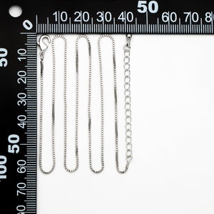 Puede incluir: Cuatro cadenas de plata de diferentes longitudes, dispuestas sobre una superficie blanca, con una regla en el fondo. Las cadenas son todas del mismo estilo, con un dise&ntilde;o de cadena de caja.
