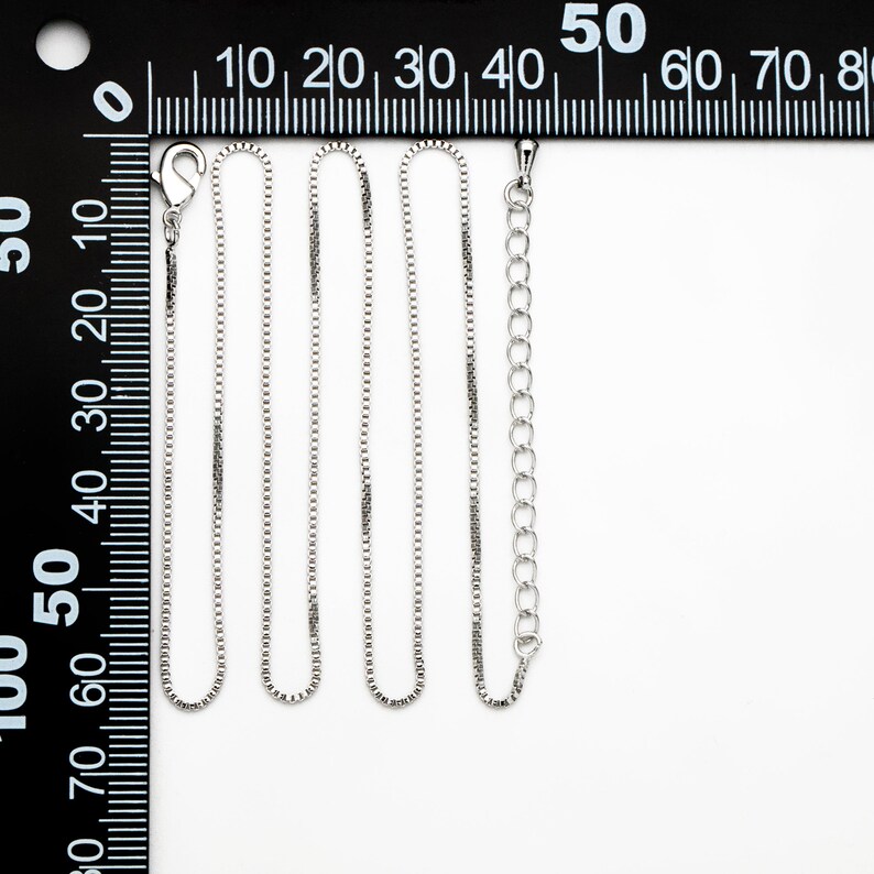 Puede incluir: Cuatro cadenas de plata de diferentes longitudes, dispuestas sobre una superficie blanca, con una regla en el fondo. Las cadenas son todas del mismo estilo, con un dise&ntilde;o de cadena de caja.