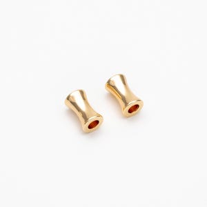 May include: Two gold-colored metal beads with a cylindrical shape and a slightly wider middle section.