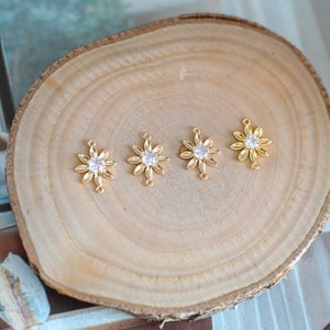 May include: Four gold-toned flower-shaped charms with clear rhinestone centers. Each charm has two loops on the back for attaching to jewelry.