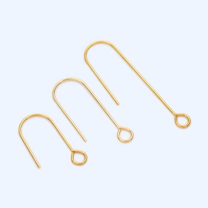 May include: Three gold-colored earring hooks of varying sizes are arranged on a light blue background. Each hook has a curved top and a loop at the bottom. The hooks are made of a shiny, metallic material.