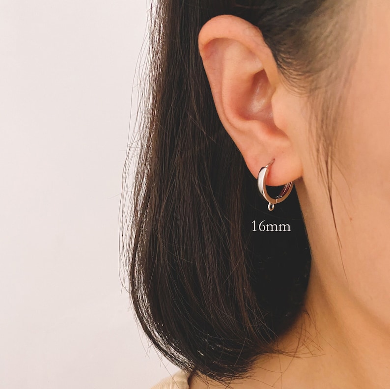 May include: Silver hoop earrings with a 16mm diameter. The earrings are shown on a person's ear.
