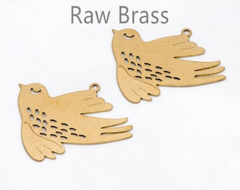 May include: Two raw brass bird charms with a flying design. Each charm has a small loop at the top for hanging and a series of small cut-out holes on the wings. The text "Raw Brass" is above the charms.