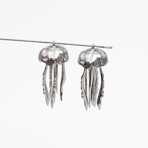 May include: A pair of silver-toned earrings shaped like jellyfish. Each earring features a detailed, textured dome with dangling tentacles.