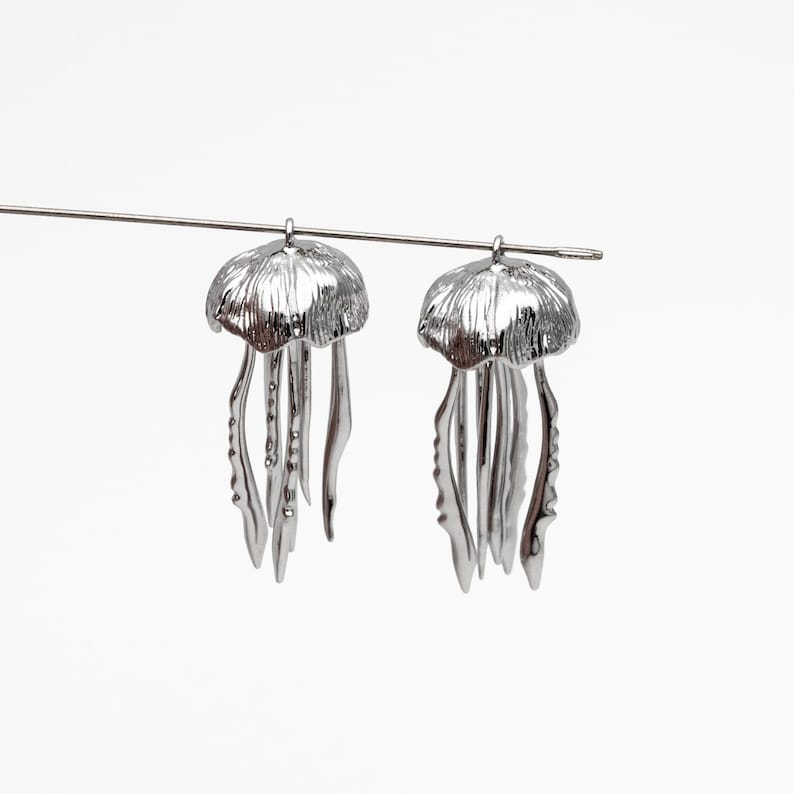 May include: A pair of silver-toned earrings shaped like jellyfish. Each earring features a detailed, textured dome with dangling tentacles.