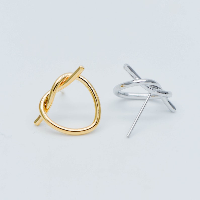 May include: A pair of minimalist earrings with a twisted knot design. One earring is gold and the other is silver.