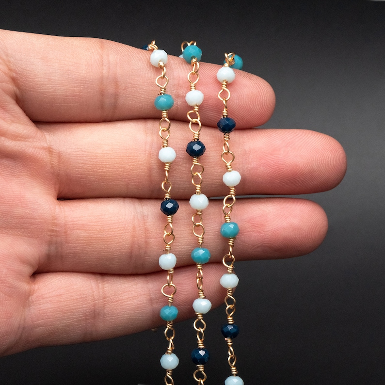 May include: Three strands of gold chain with blue, turquoise, and white beads. The beads are faceted and have a subtle shimmer.