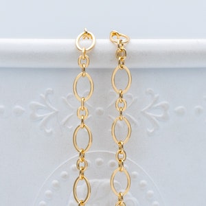 May include: Two gold chains with oval links. The chains are hanging from a white surface.