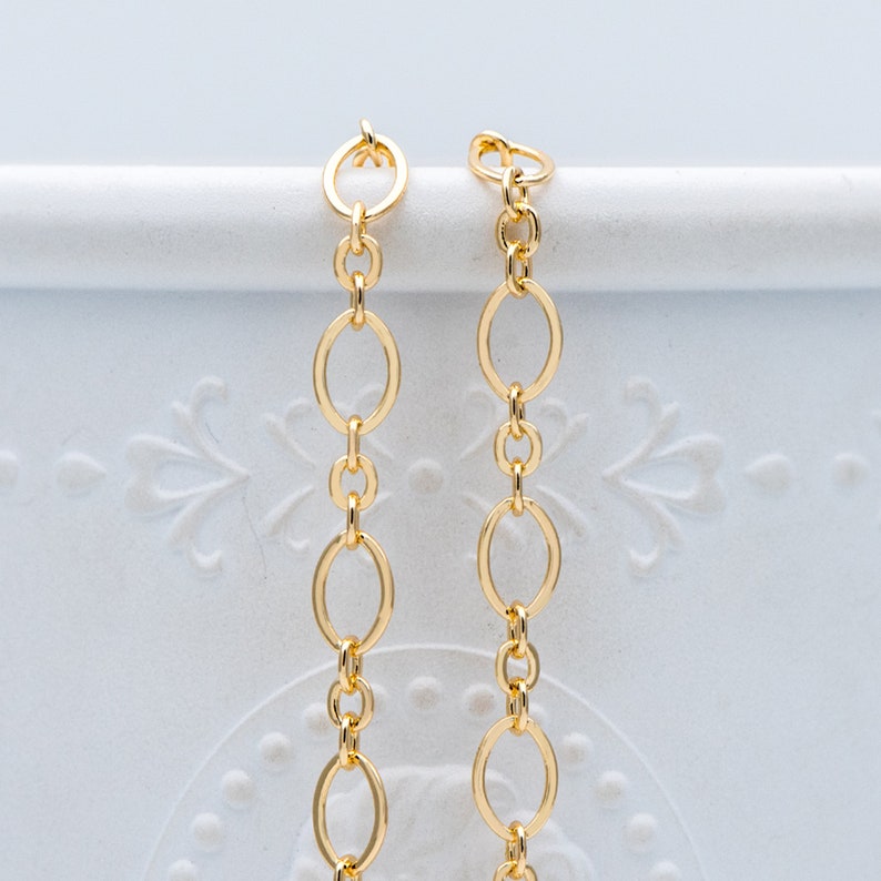 May include: Two gold chains with oval links. The chains are hanging from a white surface.
