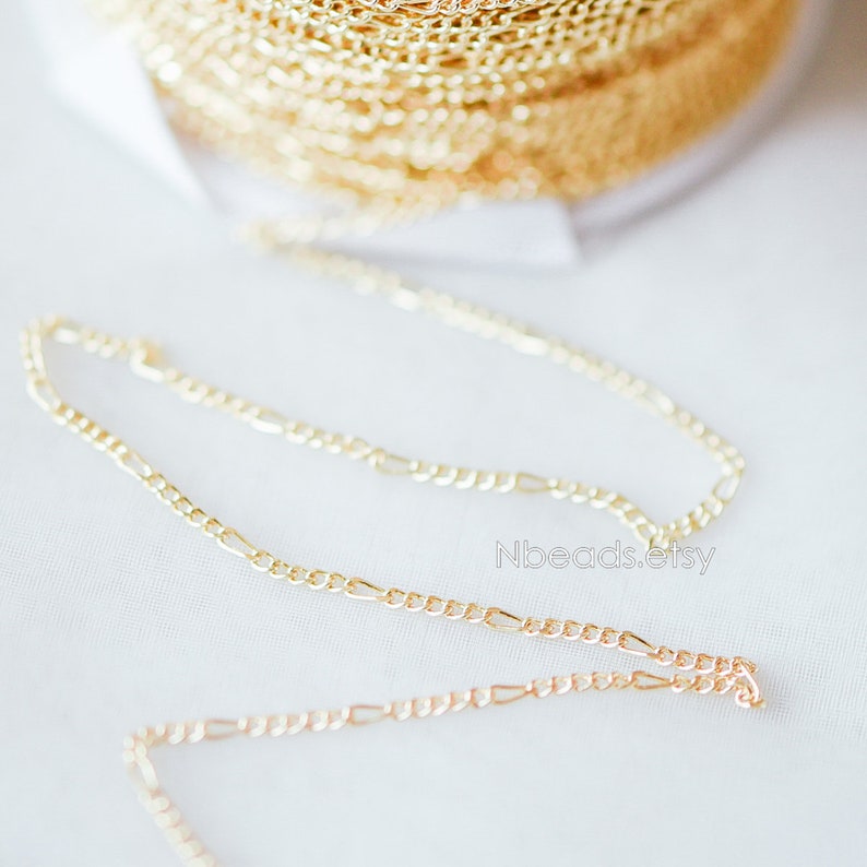 May include: Two gold chains, one on top of the other, on a white surface. The chains are both made of a thin, delicate metal and have a simple, elegant design.