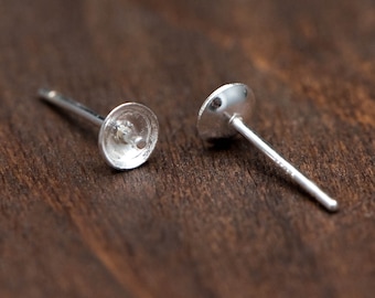 May include: Two silver earring posts with a round, flat top. The posts are designed to hold a pearl or other gemstone.