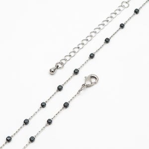 May include: A silver chain necklace with small black beads. The necklace has a lobster clasp and a silver extension chain.