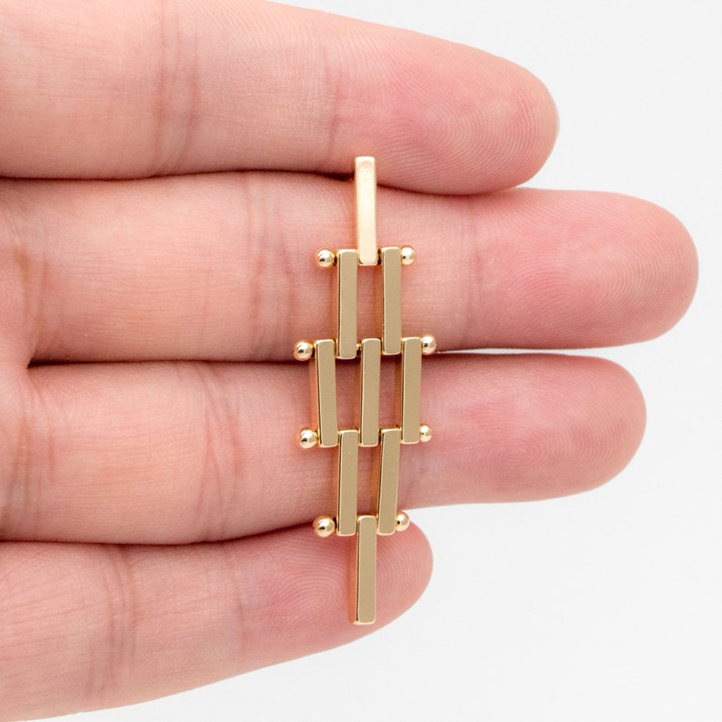 Puede incluir: Pendiente geom&eacute;trico dorado con una serie de barras conectadas y peque&ntilde;as cuentas redondas.