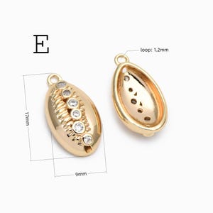 May include: Two gold-toned metal shell-shaped charms labeled E. One charm shows a front view with five embedded clear stones and a 17mm by 9mm dimension. The other charm shows a hollow back view with a 1.2mm loop measurement.