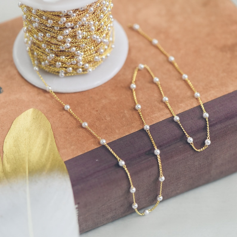 May include: A gold chain with white pearl beads. The chain is on a brown and purple surface.