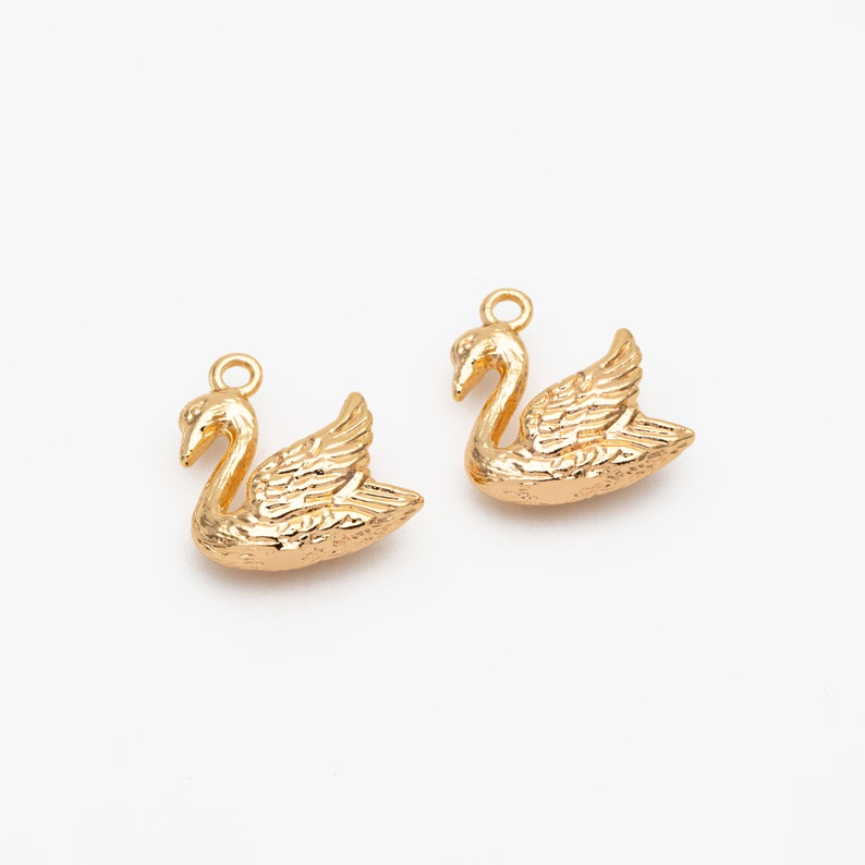 May include: Two gold swan charms with a textured surface. The charms have a loop at the top for attaching to jewelry.