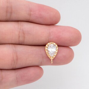 May include: Gold-tone pear-shaped pendant with a clear cubic zirconia stone surrounded by smaller cubic zirconia stones. The pendant has a loop at the bottom for attaching to a chain or other jewelry.