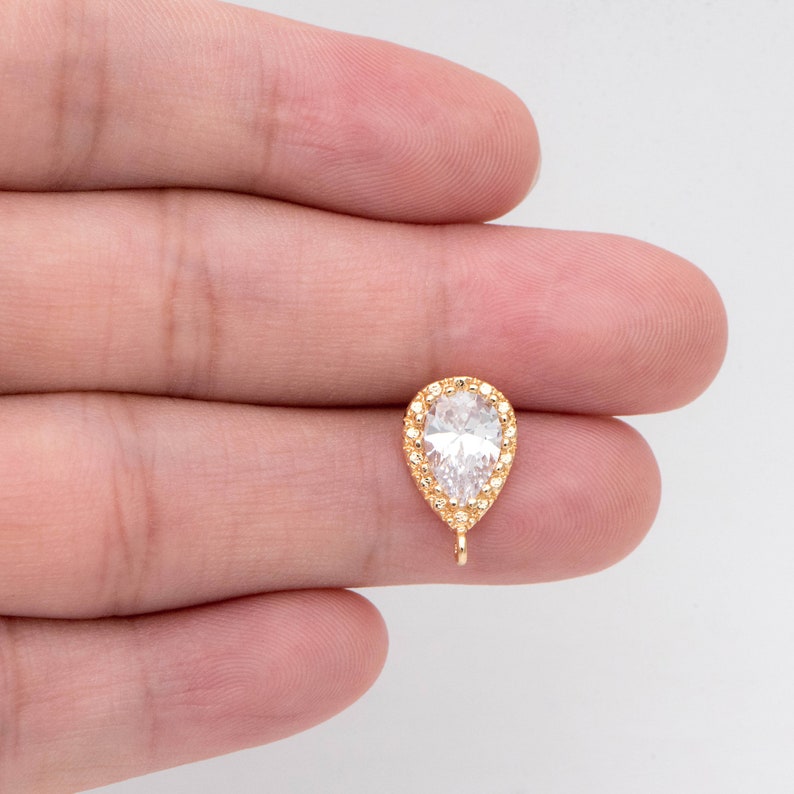 May include: Gold-tone pear-shaped pendant with a clear cubic zirconia stone surrounded by smaller cubic zirconia stones. The pendant has a loop at the bottom for attaching to a chain or other jewelry.