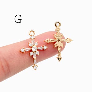 Pu&ograve; includere: Due ciondoli a forma di croce color oro. Una croce presenta un design floreale con pietre chiare e scintillanti. L'altra croce ha un design a filigrana ornato. Entrambi hanno un piccolo anello in alto per appenderli.