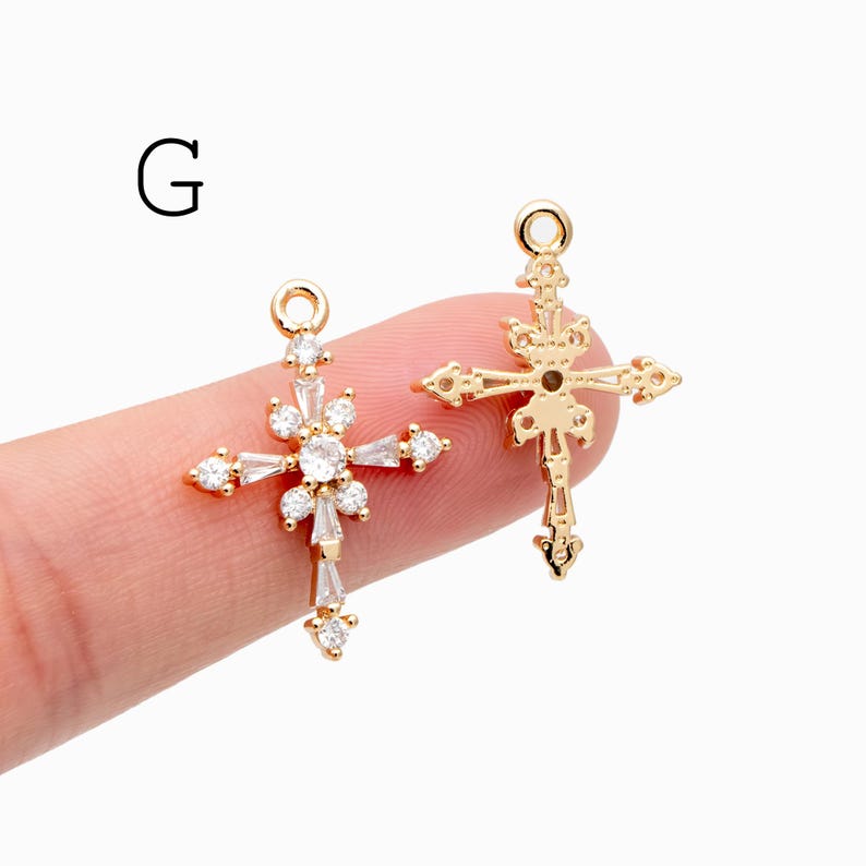 Pu&ograve; includere: Due ciondoli a forma di croce color oro. Una croce presenta un design floreale con pietre chiare e scintillanti. L'altra croce ha un design a filigrana ornato. Entrambi hanno un piccolo anello in alto per appenderli.
