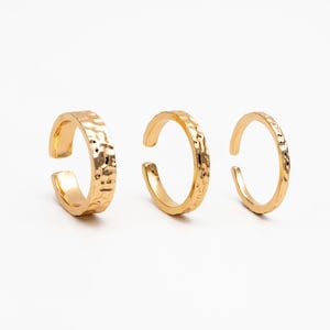 May include: Three gold-toned ear cuffs with a hammered texture. The ear cuffs are open and can be adjusted to fit different ear sizes.