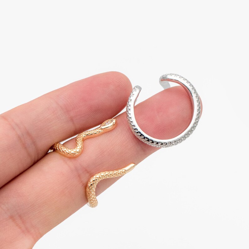 May include: Two snake-shaped rings, one gold and one silver. The silver ring is textured and the gold ring is smooth.