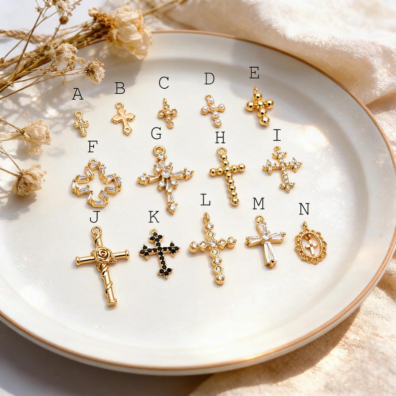 Pu&ograve; includere: Una collezione di ciondoli a forma di croce color oro con vari design, tra cui dettagli di perline, gemme e floreali. Le croci sono esposte su un piatto bianco, mostrando la loro intricata lavorazione artigianale e i diversi stili. Alcune croci hanno gemme chiare o nere.