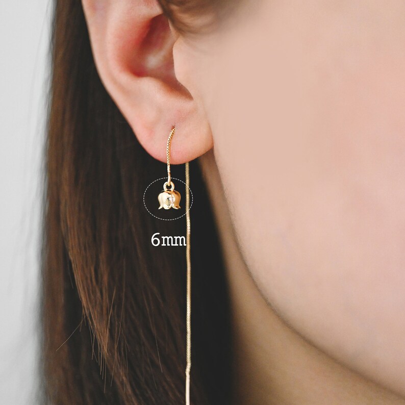 May include: Gold flower dangle earrings with a 6 mm flower charm. The earrings are long and delicate.