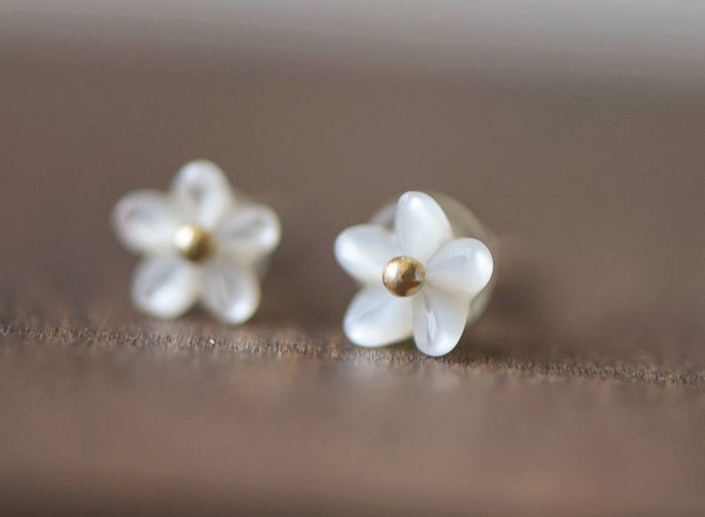 K&ouml;nnte beinhalten: Ein Paar wei&szlig;e, blumenf&ouml;rmige Ohrringe mit goldenen Zentren.