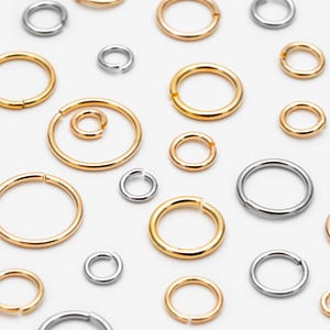 May include: A collection of assorted metal jump rings in various sizes, featuring both gold-toned and silver-toned finishes. Each circular ring has a single small opening, allowing for easy connection and assembly in jewelry making projects.