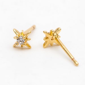 May include: A pair of gold star-shaped earrings with a small clear stone in the center of each star.