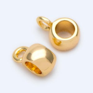May include: Two gold-colored jewelry components with a rounded, barrel-like shape and a small loop at the top. The components have a shiny, reflective surface, and are set against a white background. These are likely used for jewelry making.