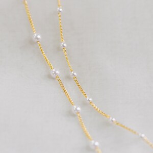 May include: Two gold chains with white pearl accents. The chains are layered on top of each other.