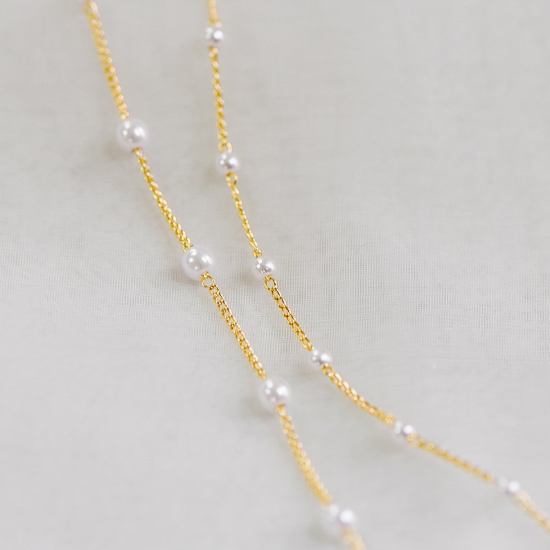 May include: Two gold chains with white pearl accents. The chains are layered on top of each other.