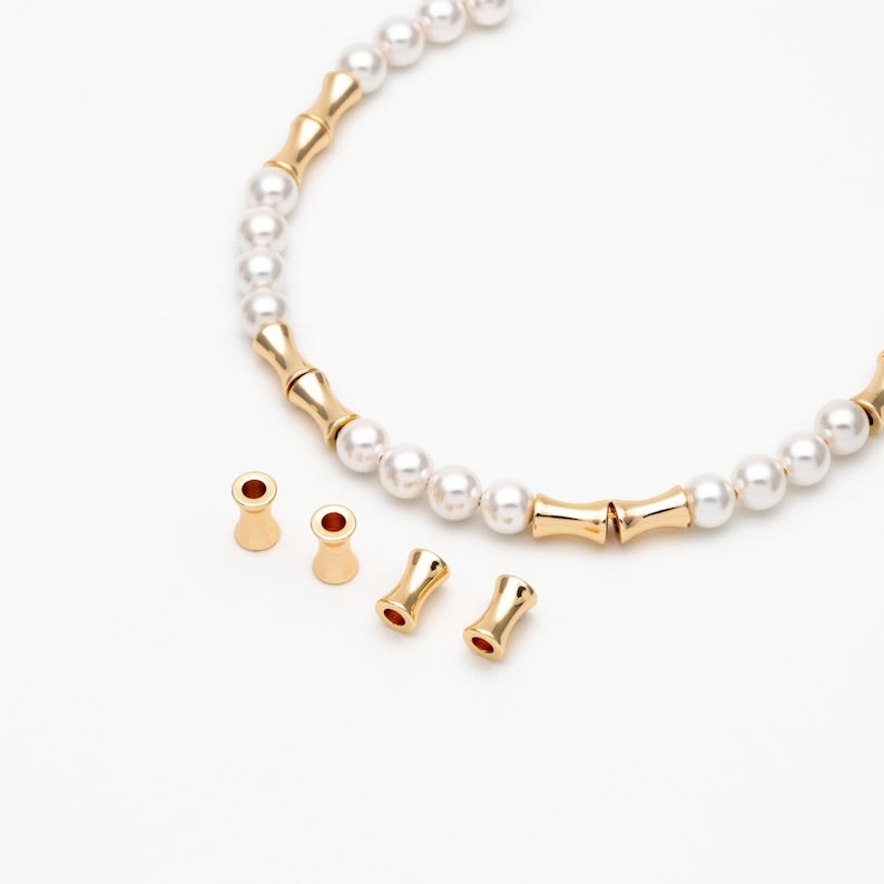 May include: A gold necklace with white pearl beads and gold spacers. The necklace is open and laid flat on a white surface. There are four gold end caps on the surface.