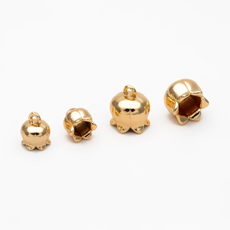 May include: Four gold-colored metal flower-shaped end caps of varying sizes. The end caps have a hole at the top for stringing.