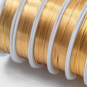 May include: Close-up of spools of gold-colored wire. The wire is wound tightly around the spools, which are white and have a smooth surface.