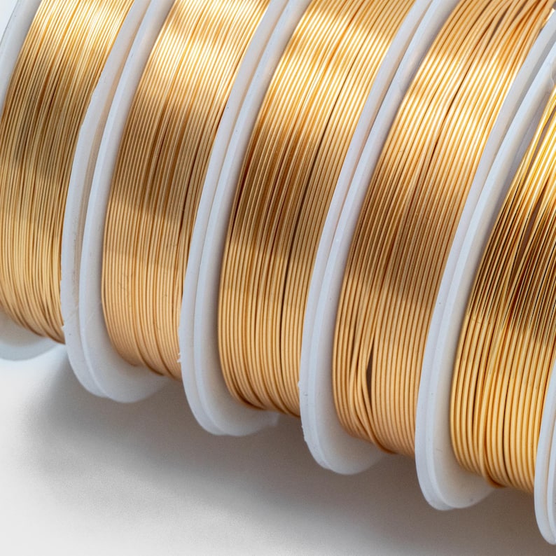 May include: Close-up of spools of gold-colored wire. The wire is wound tightly around the spools, which are white and have a smooth surface.