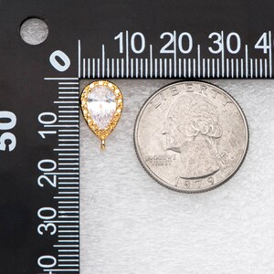May include: A gold-tone teardrop-shaped pendant with a clear cubic zirconia stone. The pendant is approximately 1 inch long and is shown next to a US quarter for size comparison.