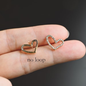 May include: A pair of gold heart-shaped earrings with a single row of clear cubic zirconia stones around the edge. The earrings are shown on a finger, and the text "no loop" is visible below the earrings.